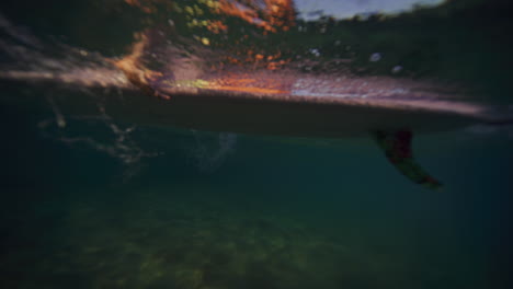 Underwater-sideview-of-surfer-paddling-longboard-with-both-arms