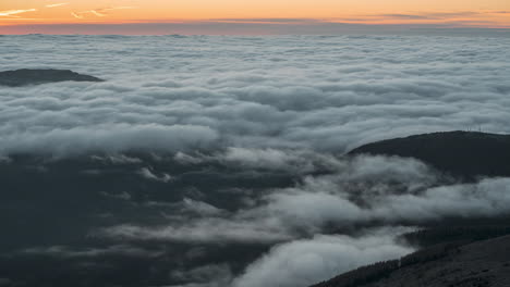Sobre-Las-Nubes-Al-Amanecer-Con-Tonos-Cálidos-Del-Cielo-Y-Silueta-De-Montaña,-Timelapse