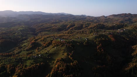 Autumn-colors-drape-Pestera-Village,-aerial-view-of-rolling-hills-under-golden-sunlight-at-dusk