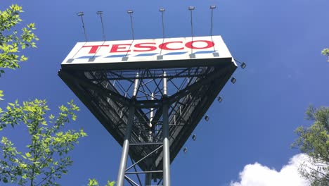 Großer-Werbebannerturm-Des-Kaufhauses-Tesco-Mit-Frühlingsbäumen-Im-Wind