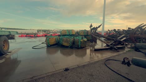 Fishing-equipment-is-laid-out-on-the-damp-asphalt-in-a-coastal-town-of-Spain,-featuring-metal-anchors-and-nets,-embodying-the-essence-of-maritime-livelihood-and-coastal-heritage