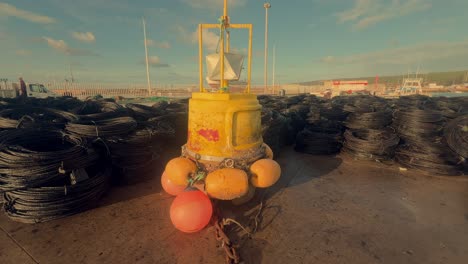 A-proud-yellow-navigation-buoy-stands-tall-on-the-dock-of-a-Spanish-coastal-fishing-village,-serving-as-a-symbol-of-maritime-safety-and-guidance-amid-the-bustling-port-activities
