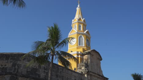 Cartagena,-Colombia-clock-tower-nestled-amidst-historic-architecture,-framed-by-palm-trees-and-under-clear-blue-skies