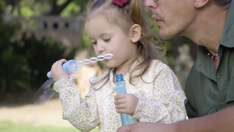 A-young-father-helps-his-adorable-little-daughter-to-play-with-bubbles-in-the-city-park