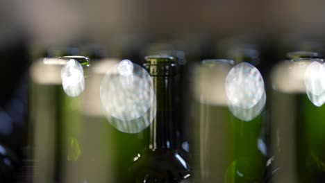 Green-glass-wine-bottle-necks-being-moved-in-place-by-a-conveyor-belt-in-Vignonet-France-before-the-filling-process,-Close-up-shallow-depth-shot