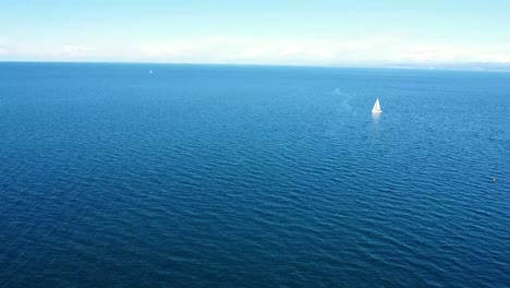 Empuje-Aéreo-Desde-La-Costa-Al-Mar-Con-Velero-En-El-Fondo-Del-Mar-Azul