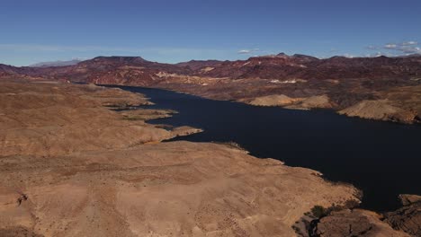 Aerial-View-of-Colorado-River-with-Desert-on-One-Side,-Red-Rock-Mountains-and-Plateaus-on-the-Other