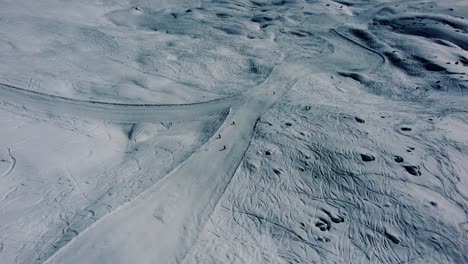 People-going-downhill-on-white-ski-slope,-aerial