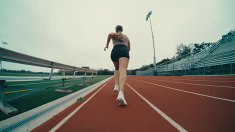 Female-track-athlete-running-on-red-track-at-outdoor-football-field-in-extreme-slow-motion,-4k-800fps-runner-fisheye-follow-from-behind
