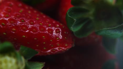 Macro-detailed-video-of-a-group-of-strawberries,-red-strawberry,-green-leaf,-tiny-seeds,-on-a-rotating-reflection-stand,-smooth-movement