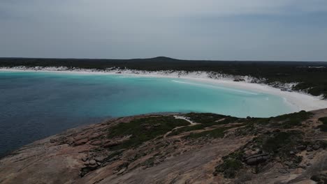 Drone-flying-over-rocky-hills-with-Wharton-Beach-in-background,-Western-Australia