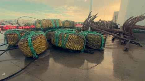 Fishing-equipment-lies-atop-the-damp-asphalt-in-a-Spanish-coastal-town,-featuring-metal-anchors-and-nets,-symbolizing-the-essence-of-maritime-livelihood-and-coastal-tradition