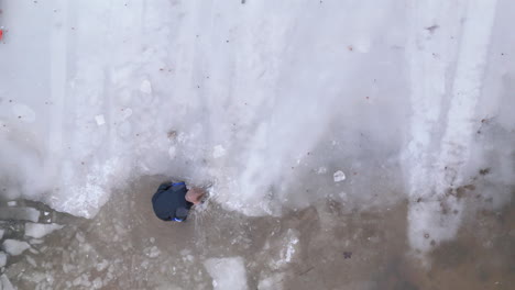 Buceador-De-Hielo-Con-Traje-Seco-Rompe-El-Borde-Del-Hielo-Del-Lago-Para-Abrir-El-Punto-De-Entrada,-Drone-Superior