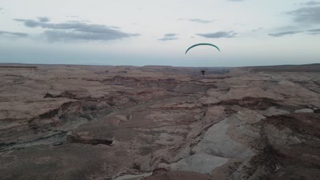 In-the-vast-skies-of-Utah,-USA,-a-lone-paraglider-gracefully-maneuvers,-gliding-peacefully-above-the-rugged-and-arid-terrain,-embodying-freedom-amid-the-expansive-desert-scenery