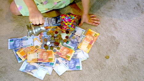 Top-view-of-girl-throwing-out-coins-onto-spread-out-South-African-rand-banknotes