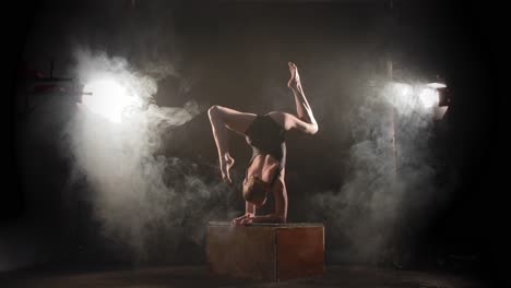 Bendy-contortionist-doing-scorpion-pose-on-box-between-spotlights-and-smoke