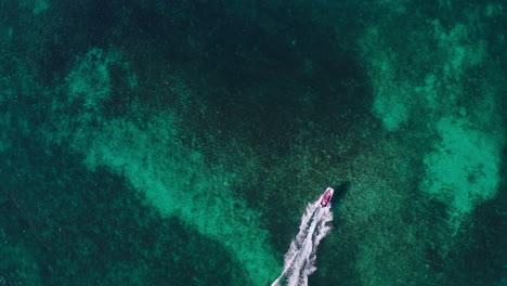 Top-down-aerial-view-of-a-speedboat-riding-through-shallow-blue-waters