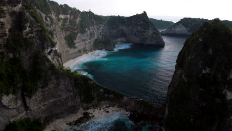 Drone-flying-between-high-and-rocky-cliffs-of-Diamond-Beach-at-sunrise,-Nusa-Penida-island,-Bali-in-Indonesia