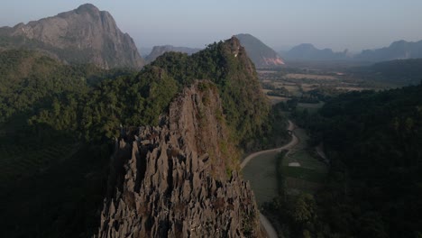 drone-shot-of-jagged-cliffs-and-country-road-in-Vang-Vieng,-the-adventure-capital-of-Laos