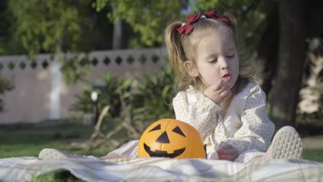 Close-up-of-adorable-little-girl-eating-sweeties-from-Halloween-pumpkin-in-the-city-park
