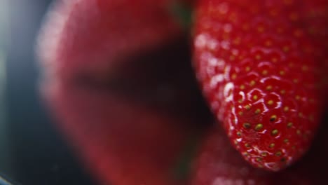 Macro-epic-video-of-a-pile-of-strawberries,-red-strawberry,-green-leaf,-tiny-seeds,-on-a-rotating-reflection-stand,-smooth-movement