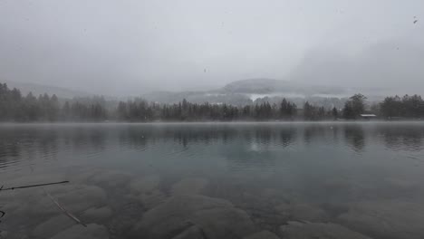 Snow-is-falling-on-Lake-with-Crystal-Clear-Water-with-Forest-in-Background-in-Austria,-Europe