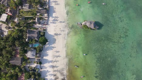 Aerial-view-looking-down-over-rock-restaurant-Zanzibar-during-golden-hour-with-palm-tree-shadows-on-white-sandy-African-resort-shoreline