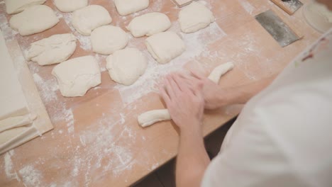 Baker-rolling-fresh-dough-for-baguette,-over-shoulder-slow-motion