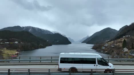 Mini-tour-bus-crossing-bridge,-foggy-Veafjord-Fjord-in-background,-aerial-tracking