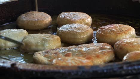 Freshly-made-Xian-Bing-cooking-in-hot-oil-pan,-a-stall-vendor-flipping-savoury-minced-pork-meat-pie-pastry-using-kitchen-tongs,-pan-frying-until-golden-brown,-close-up-shot-of-popular-Asian-food