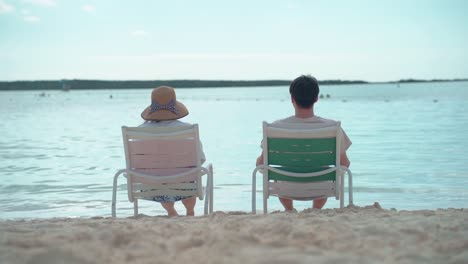 Couple-sitting-in-chairs-on-the-beach-looking-out-to-sea-slow