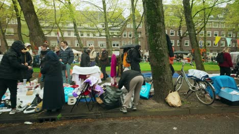 Juguetes-Y-Artículos-Expuestos-En-El-Suelo-En-Apollolaan-En-Amsterdam-Con-Gente-Caminando-Junto-A-Ellos.