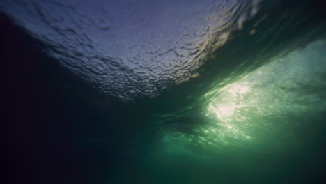 Underwater-view-of-breaking-wave-sparkling-with-sunlight-and-surfer