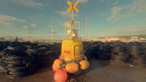 A-sturdy-yellow-navigation-buoy-stands-tall-on-the-dock-of-a-coastal-Spanish-fishing-village,-acting-as-a-beacon-of-maritime-safety-and-guidance-amidst-the-lively-port-activities