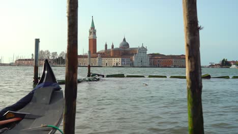 Schwimmende-Gondeln,-Die-In-Den-Frühen-Morgenstunden-An-Holzmasten-In-Venedig-Festgeschnallt-Sind,-Mit-Der-Wunderschönen-Kirche-San-Giorgio-Maggiore-Im-Hintergrund