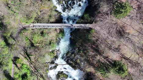 The-scenic-aerial-perspective-of-a-charming-footbridge-spanning-the-waters-of-Seerenbachfälle,-situated-between-Amden-and-Betlis-in-Switzerland