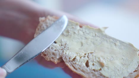 Close-up-of-a-hand-spreading-butter-on-bread-slice,-soft-focus,-in-slow-motion