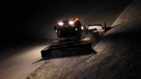 Rasuradora-De-Nieve-Trabajando-De-Noche-En-Los-Dolomitas,-Alpes-Italianos,-Con-Luces-Brillantes-Y-Un-Rastro-Claro-Detrás