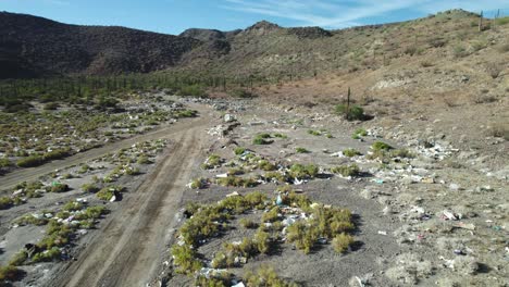 Waste-Scattered-Along-the-Roadside-in-the-Desert-Landscape-of-Mulege,-Baja-California-Sur,-Mexico---Aerial-Pullback-Shot