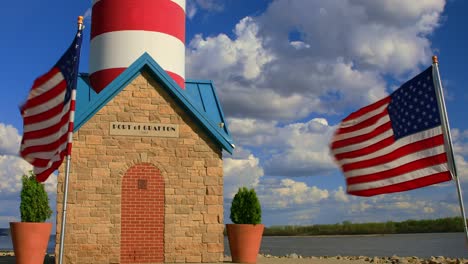 Port-Of-Grafton-Lighthouse-with-American-Flags-Waving-in-the-Wind-Against-Blue-Skies-and-Clouds,-Illinois,-USA