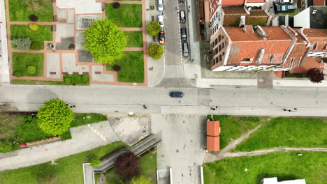 Vista-Aérea-De-Arriba-Hacia-Abajo-De-Un-Entorno-Urbano-Pintoresco,-Con-árboles-Verdes-Vibrantes-Que-Se-Destacan-Entre-Edificios-Con-Techos-Rojos,-Un-Parque-Urbano-Ordenado-Y-Calles-Entrecruzadas,-Una-Vida-Urbana-Organizada-Y-Tranquila.