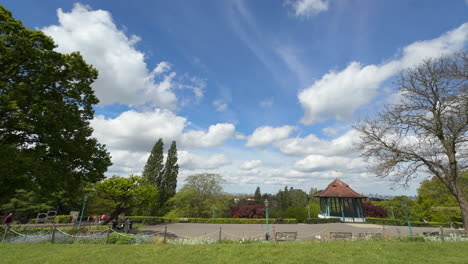 Horniman-Gardens,-Forest-Hill,-London,-time-lapse,-blue-sky,-fast-moving-white-clouds,-band-stand,-slow-pan-left-to-right