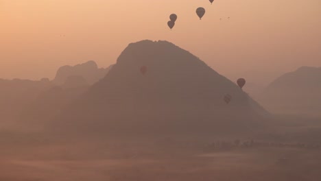 hot-air-balloons-rising-over-mountain-during-sunrise-in-Vang-Vieng,-the-adventure-capital-of-Laos