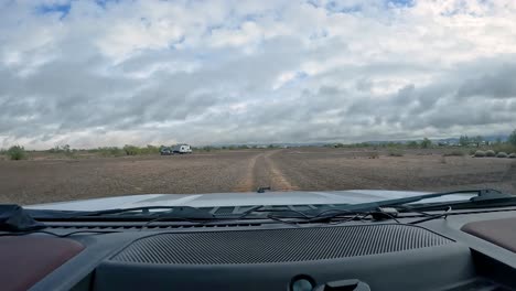 POV-driving-on-gravel-trail-through-the-Sonoran-desert-in-southwest-Arizona-towards-groups-of-dispersed-campers-on-a-cloudy-winter-day