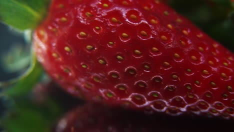 Macro-detailed-video-of-a-pile-of-strawberries,-red-strawberry,-green-fruit,-tiny-seeds,-on-a-rotating-reflection-stand,-smooth-movement
