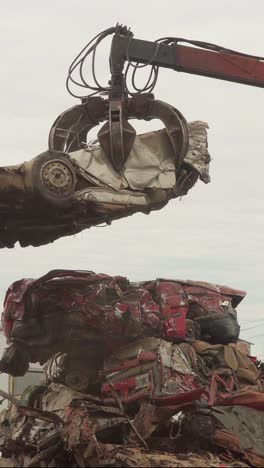 Vertical-view-of-a-hydraulic-claw-placing-a-crushed-car-on-a-pile-in-a-junkyard