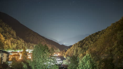 Nachtansicht-Eines-Bergdorfes-Unter-Einem-Sternenhimmel,-Warm-Leuchtende-Lichter-Zwischen-Den-Bäumen,-Zeitraffer