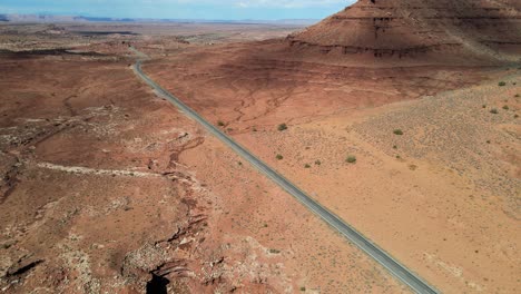 Die-Luftaufnahme-Zeigt-Eine-Gerade-Straße,-Die-Durch-Die-Weite-Wüstenlandschaft-Des-Monument-Valley-Führt,-Das-An-Der-Grenze-Zwischen-Arizona-Und-Utah-In-Der-Nähe-Von-Mexican-Hat,-Utah-Liegt.