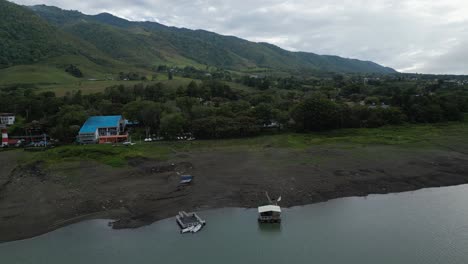 Vista-Aérea-De-La-Costa-Del-Lago-Con-árboles-Y-Montañas.