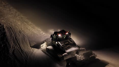Bulldozer-clearing-snow-at-night-in-the-Dolomites,-Italy,-with-bright-lights-and-snowy-gusts